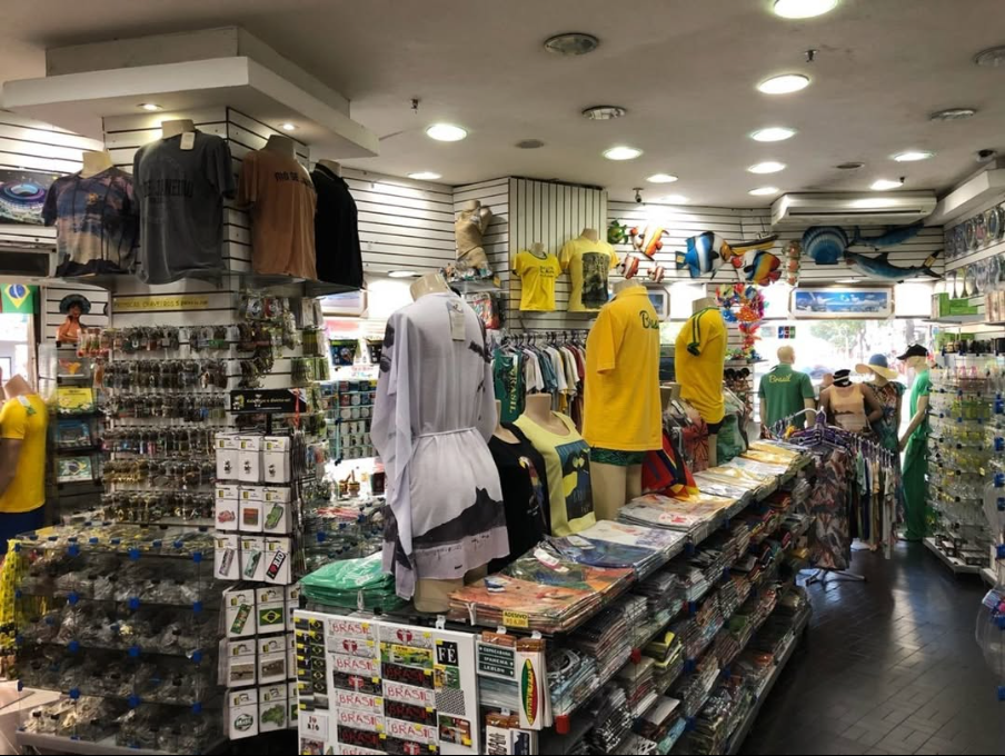 Interior da loja Tropicale, com araras de camisetas, prateleiras de suvenires e provadores
